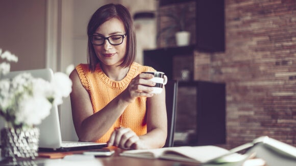 woman with orange top and coffee cup working from home