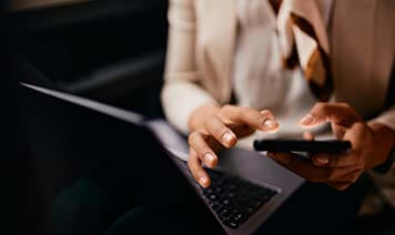 Hands typing on phone and laptop
