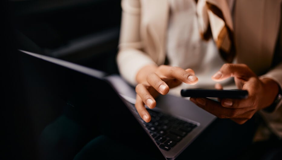 person holding smartphone with laptop open