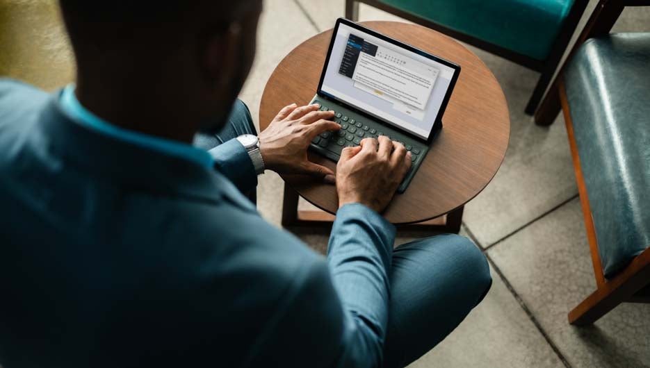 Young African businessman working on a digital tablet while sitting alone in an office lounge area