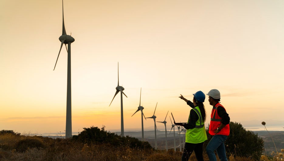 Young maintenance engineer team working in wind turbine farm at sunset