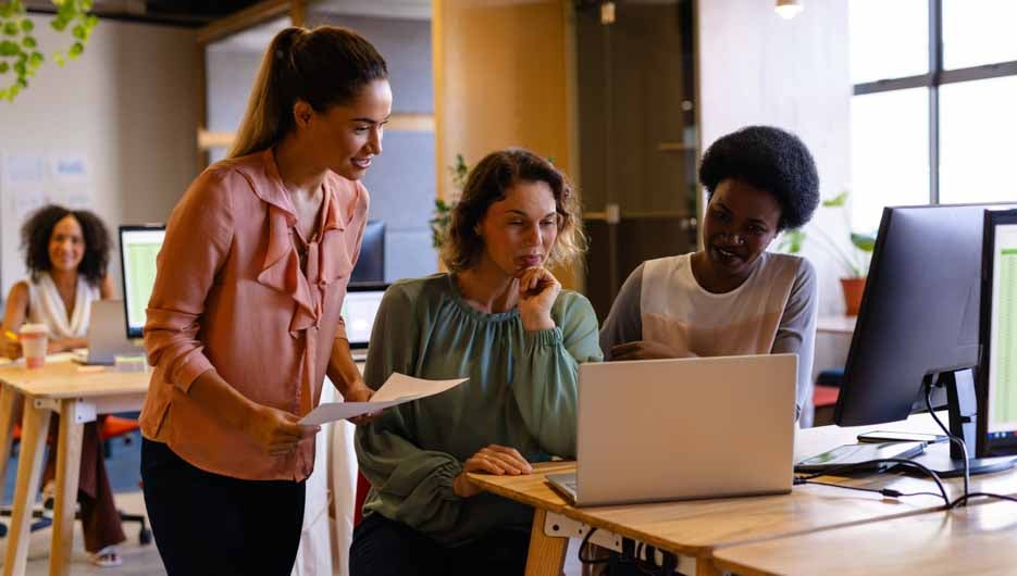 Diverse female colleagues in discussion using laptop in casual o
