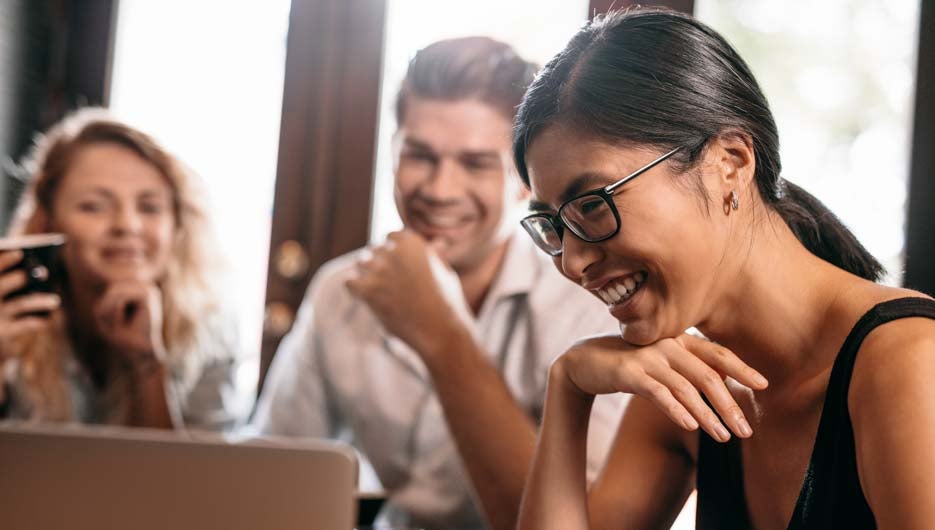 Close up shot of smiling asian woman looking at laptop with friends in cafe. Friends in coffee shop looking at laptop and smiling.